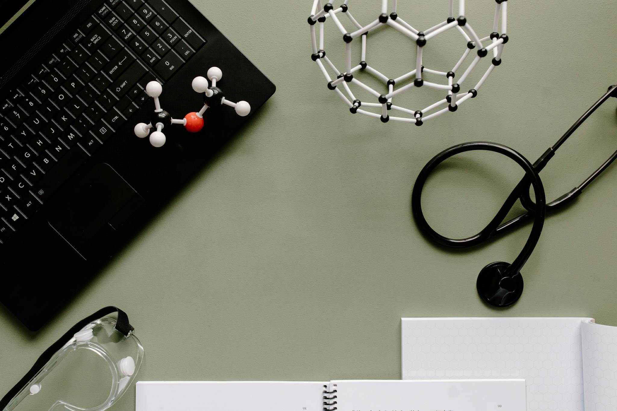 Medical workspace with laptop, molecules, and stethoscope on green background.